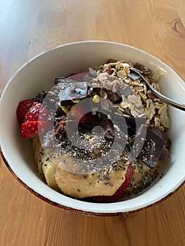 Protein Bowl with Chia Seeds, Banana, Strawberry, Rolled Oats and Bitter Chocolate Pieces on Wooden Table for Breakfast