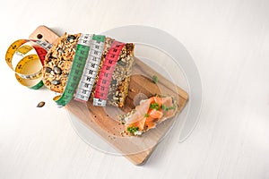 Protein bread with tape measure and a sandwich with salmon on a cutting board and a white table, slimming concept with low carb or