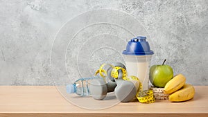 Protein cocktail, dumbbells, measuring tape, water bottle and fresh fruits on wooden table