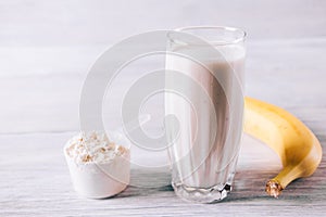 Protein cocktail in a glass, scoop and banana on a white wooden