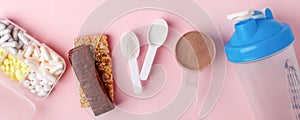 Protein powder, scoop, energetic musli bars, vitamin pills, gainer, shaker on pink background - concept of sport diet, healthcare