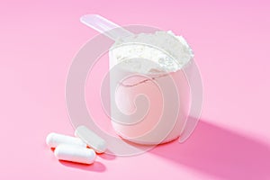 Protein scoop and capsules on pink background close-up