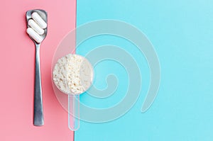 Protein scoop and capsules on pink and blue background close-up.
