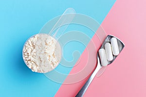 Protein scoop and capsules on pink and blue background close-up, top view