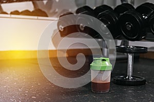 Protein shake and dumbbells at the gym. Fitness nutrition drink and heavy weights.