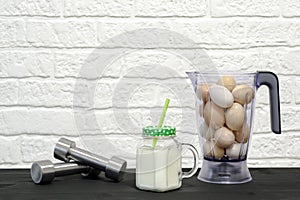 Protein shake in a mug against the background of a blender bowl with chicken eggs and dumbbells against a white wall