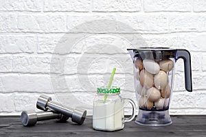 Protein shake in a mug against the background of a blender bowl with chicken eggs and dumbbells against a white wall