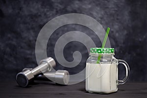 Protein white cocktail in a mug on a background of dumbbells on a dark background. Background