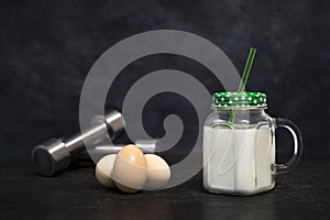 Protein white cocktail in a mug and chicken eggs on a dark background with dumbbells. Background