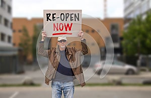 Protester with cap and sunglasses demonstrate against stay-at-home orders due to the COVID-19 pandemic carrying sign saying Re-ope