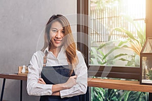Protrait of young Asian female barista welcome her customer to coffee shop in warm light afternoon with a beautiful smile.