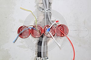 Protruding electric wires and cables in holes inside grey cement wall to prepare for electricity in the House under construction.