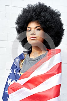 Proud African woman stand on white background wrapped in usa flag, portrait.