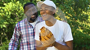 Proud afro-american dad encouraging teenage son playing baseball, togetherness