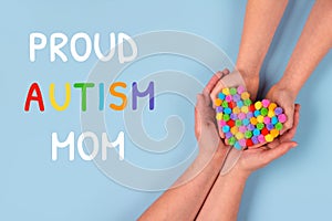Proud Autism Mom and World Autism Awareness Day concept - autistic child`s hands supported by mother holding multicolored heart o
