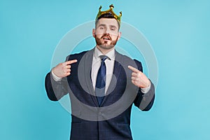 Proud bearded man wearing official style suit egoistically looking at camera, posing with crown on