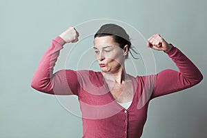 Proud beautiful 40s woman admiring her flexing muscles