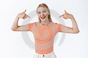 Proud, boastful good-looking stylish young woman with blond hair, tattoos, standing striped t-shirt, pointing herself as