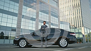 Proud car owner posing at black automobile on street. Businessman standing car