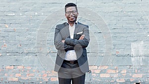 Proud and confident young African American businessman in suit and glasses smiling and crossing his arms. Financial