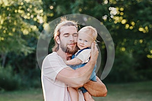 Proud father hugging embracing toddler baby boy outdoor. Young parent holding child son in arms. Authentic lifestyle tender moment