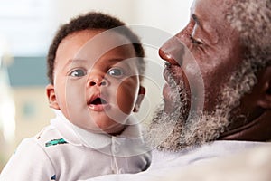 Proud Grandfather Cuddling Baby Grandson In Nursery At Home