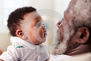 Proud Grandfather Cuddling Baby Grandson In Nursery At Home