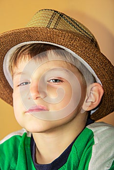 A proud and greedy boy in a straw hat with a haughty facial expression looks into the camera on a yellow background