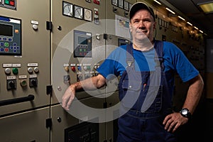 Proud and happy mechanic / chief engineer, posing with his arms crossed in the engine room of an industrial cargo ship