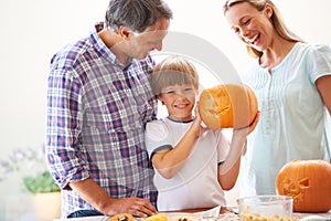 Proud of his pumpkin carving. Portrait of a little boy holding his jack-o-lantern with hi parents on either side of him.