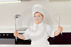 Proud little boy chef holding up his utensils