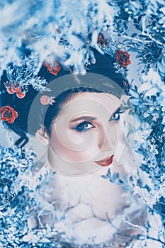 Proud majestic queen of winter and eternal cold in long white dress with dark collected hair adorned with frozen roses