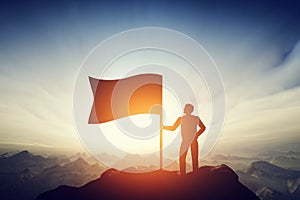 Proud man raising a flag on the peak of the mountain. Challenge, achievement