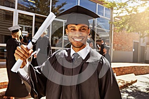 Proud of my scholastic success. Portrait of a smiling university student holding his diploma outside on graduation day.