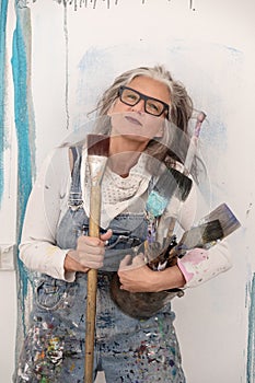 Proud older artist woman, in her fifties with grey hair and black glasses and many paintbrushes