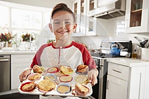 Proud pre-teen Hispanic boy standing in kitchen presenting the cakes heï¿½s made to camera, close up