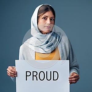 Proud. Studio portrait of an attractive young woman holding up a sign reading PROUD against a grey background.