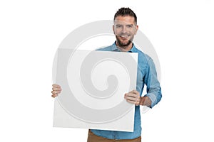 Proud unshaved man holding board and presenting advertisement