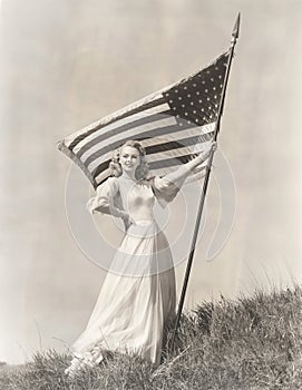 Proud woman in gown holding American flag on hill