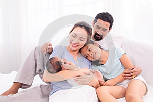Proudly Asian man hug wife and 2 kids with love, care, protection, adorable daughter lie down on father`s bosom or chest looking