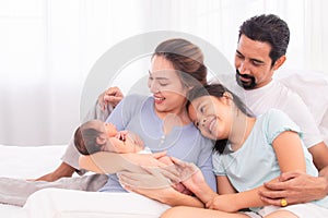Proudly Asian man hug wife and 2 kids with love, care, protection, adorable daughter lie down on father`s bosom or chest looking