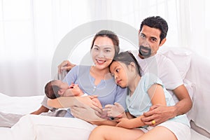 Proudly Asian man hug wife and 2 kids with love, care, protection, adorable daughter lie down on father`s bosom or chest looking