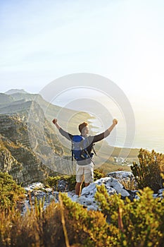 Prove to yourself you can. a young man cheering while hiking up a mountain.