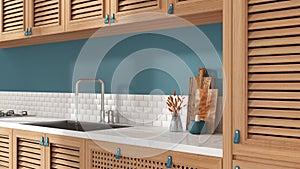 Provencal wooden kitchen in white and blue tones, close up. Cabinets with shutters and rattan drawers, leather handles, sink,