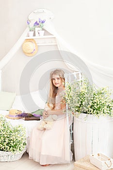 Provence. Portrait of a little girl on the bed in a bright bedroom in the morning. Blonde cute girl with long hair hugs a teddy be