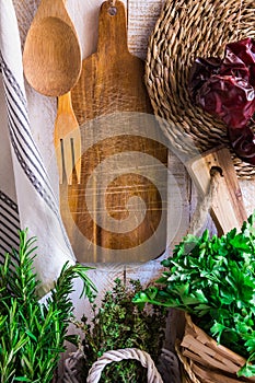 Provence style kitchen interior, white wooden wall, cutting board, utensils, rattan coaster, linen towel, fresh garden herbs rosem