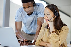 Providing coaching to his customer service team. two businesspeople working together on a laptop in a call centre.