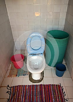 Provisional porcelain toilet without flushing mechanism installed in room without pipes or plumbing, green barrel with water near