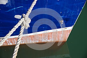 Prow of boat tied up in water with knotted rope