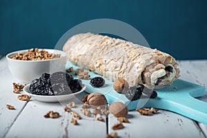 Prune-nut meringue roll on a blue cutting board on a white vintage wooden kitchen table